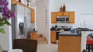 A modern kitchen with wooden cabinets, stainless steel appliances, and a dining area with a wicker chair. - Perfect 5 bedroom family home with Pool & Jacuzzi near Disney World (Davenport)