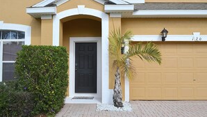 A house with a black front door, a garage door, and a small palm tree in the front yard. - Perfect 5 bedroom family home with Pool & Jacuzzi near Disney World (Davenport)