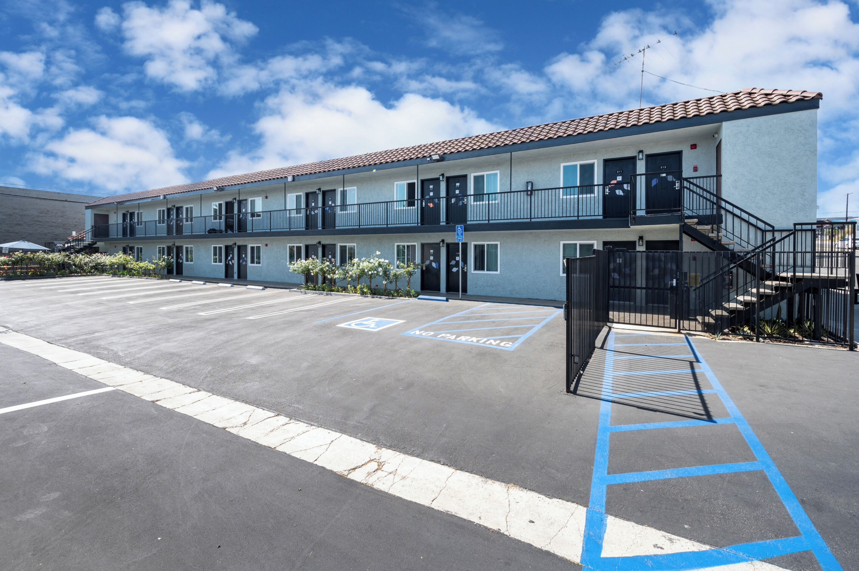 Un motel de varios pisos con estacionamiento, espacios designados para discapacitados y una escalera que conduce a la entrada.