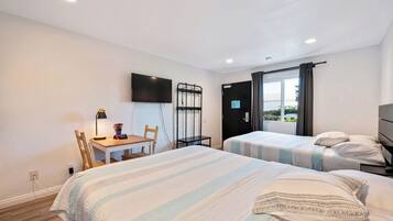 A hotel room with two beds, a desk with a chair, a TV mounted on the wall, and a window with curtains.