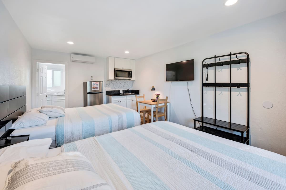 A hotel room with two beds, a kitchenette, a TV, and a seating area.