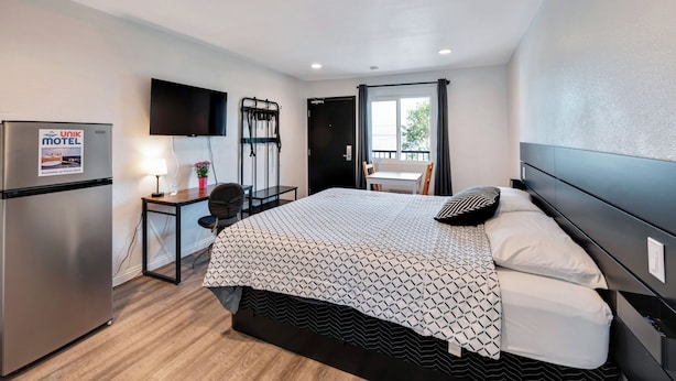 Une chambre d’hôtel comprenant un lit, un bureau avec une chaise, un téléviseur fixé au mur, une fenêtre avec des rideaux et un mini-bar.