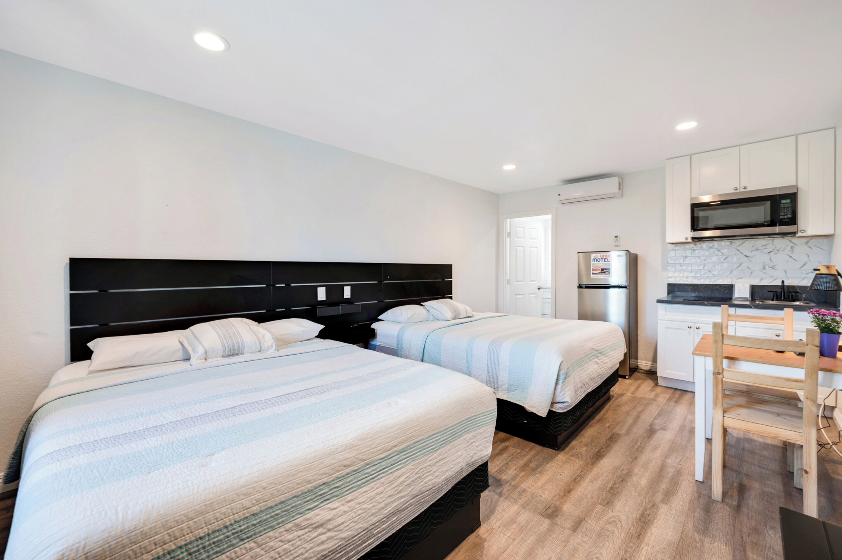 A hotel room with two beds, a kitchenette, and a small dining area.