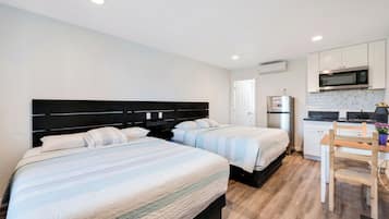 A hotel room with two beds, a kitchenette, and a small dining area.