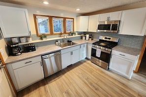 A modern kitchen with white cabinets, stainless steel appliances, and a wooden floor.