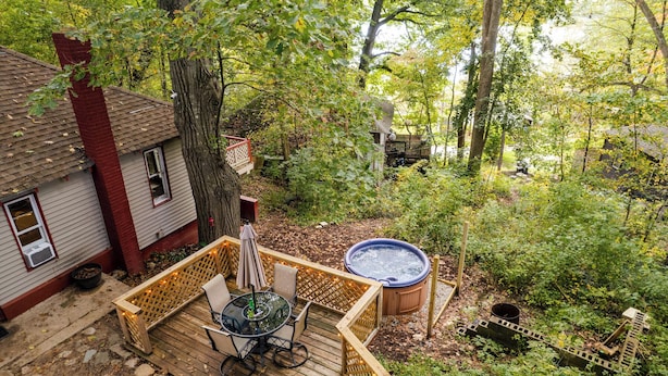 Een houten terras met een jacuzzi, omringd door een tuin en bomen.