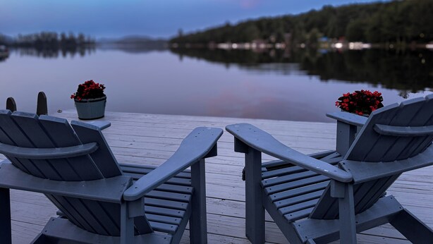 A wooden deck with two Adirondack chairs and two potted plants with red flowers. - West Bay Hideaway on Big Moose Lake (Webb)