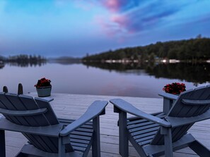 A wooden deck with two Adirondack chairs and two potted plants with red flowers. - West Bay Hideaway on Big Moose Lake (Webb)