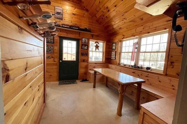 A wooden cabin interior with a kitchen area, a dining table, and a bench.