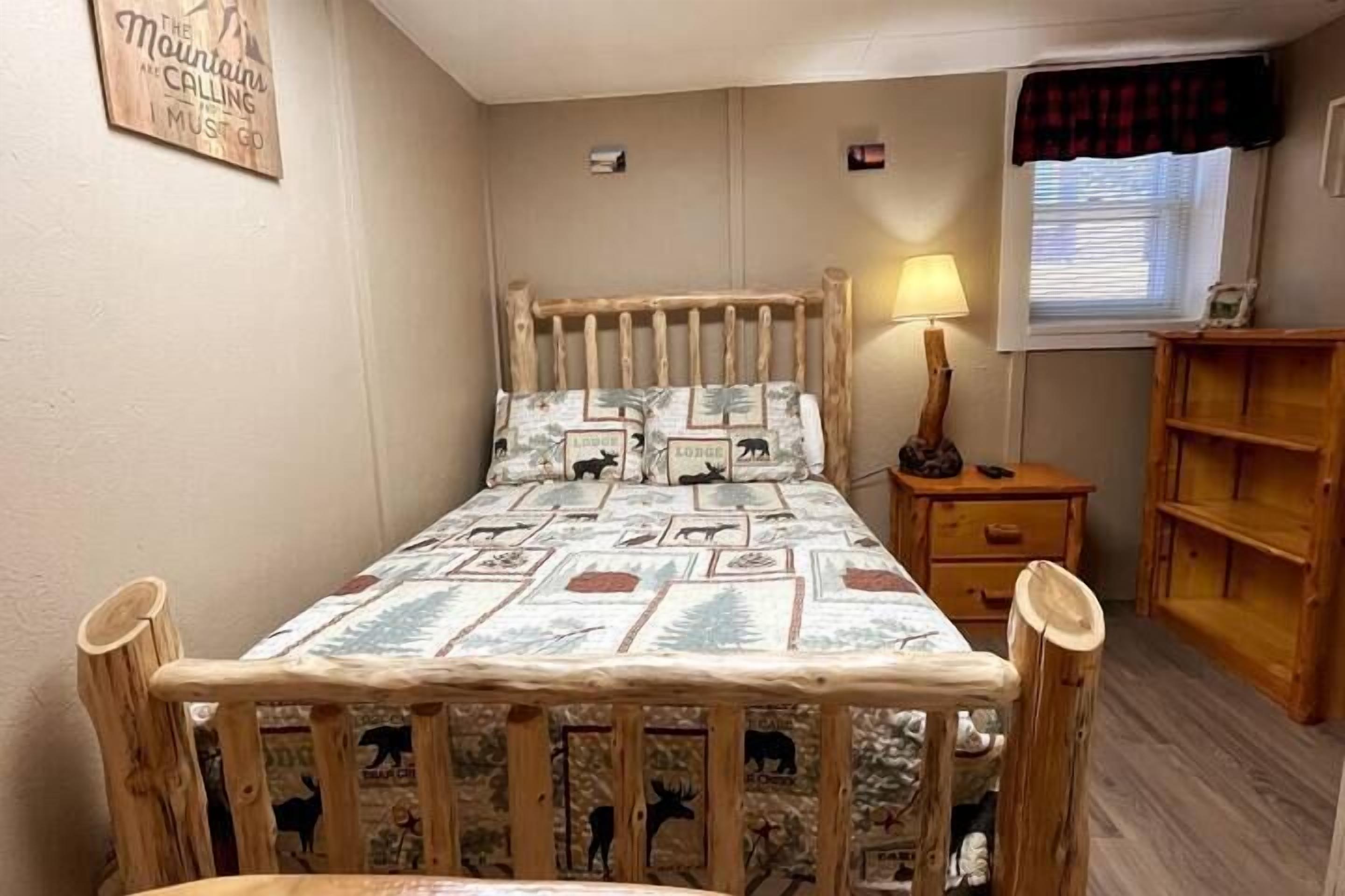 Une chambre à coucher avec un cadre de lit en bois, une couvre-lit à motifs, une table de chevet avec une lampe, une fenêtre donnant sur un paysage agréable et une étagère en bois.