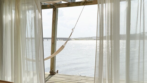 A wooden deck with a hammock, white curtains, and a bed with a brown blanket. - Laguna Garzón LODGE (José Ignacio)