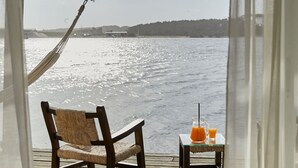 A wooden deck with a wicker chair and a small table with drinks, overlooking a body of water. - Laguna Garzón LODGE (José Ignacio)