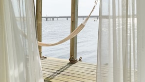 A wooden deck with a hammock, white curtains, and a view of the water and a bridge. - Laguna Garzón LODGE (José Ignacio)