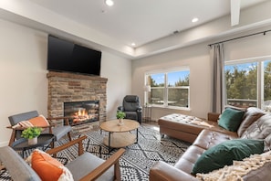 A modern living room with a fireplace, leather sofa, and a flat-screen TV mounted above the fireplace. - Lakefront Rooftop Hangout Hot Tub Fire Pit Arcades (Branson)
