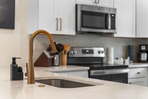 A modern kitchen with stainless steel appliances, a white countertop, and a gold faucet. - Lakefront Rooftop Hangout Hot Tub Fire Pit Arcades (Branson)