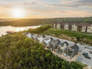 A multi-story hotel with a rooftop pool, surrounded by dense greenery and a lake. - Lakefront Rooftop Hangout Hot Tub Fire Pit Arcades (Branson)