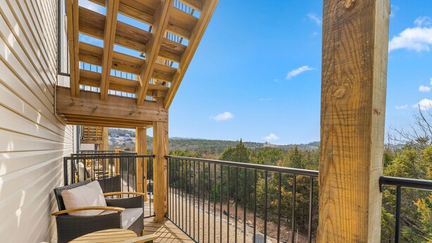 Un balcon agrémenté de meubles en osier, une pergola en bois et une vue sur le paysage.