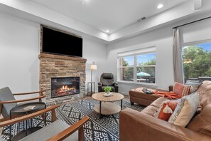 A modern living room with a stone fireplace, leather sofa, and a large window with a view. - Lakefront Rooftop Hangout Hot Tub Fire Pit Arcades (Branson)