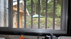 A window with vertical bars, a view of a building with a green umbrella, and outdoor greenery.