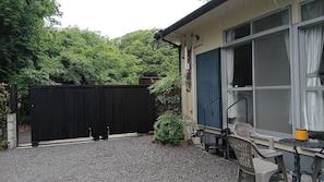 A residential property with a gravel driveway, a black fence, a patio with outdoor furniture, and a large window with curtains.