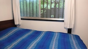 A bedroom with a bed, a window with curtains, and a view of greenery outside.