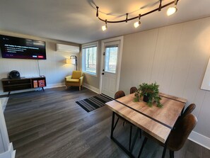 Ein modernes Wohnzimmer mit Flachbildfernseher, einem gelben Sessel, einem Holztisch und einer Topfpflanze.