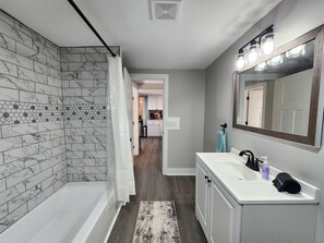 Ein modernes Badezimmer mit Dusche, Waschbecken und Spiegel sowie Blick zur Küche.