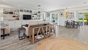 Un salon spacieux avec un canapé, une table basse et un téléviseur. Il y a également un coin repas avec une table et des chaises. Les murs de la pièce sont blancs et le sol est en bois.