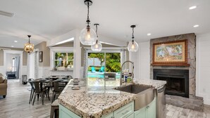 Une cuisine spacieuse dotée d’un grand îlot central, d’une cheminée en pierre et de luminaires suspendus.