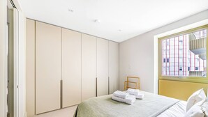 Une chambre à coucher avec un lit, une armoire et une fenêtre donnant sur des immeubles.