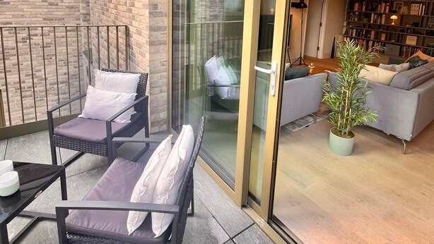 Un espace de vie moderne avec une façade en briques, une porte vitrée donnant sur un intérieur chaleureux, comprenant un canapé, une table basse et une plante en pot.
