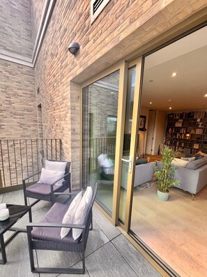 Un espace de vie moderne avec une façade en briques, une porte vitrée donnant sur un intérieur chaleureux, comprenant un canapé, une table basse et une plante en pot.