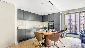 Une cuisine moderne avec des meubles de couleur sombre, une table ronde en bois et quatre chaises.