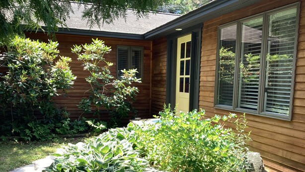 A wooden house with a stone pathway, green plants, and a door with a window.