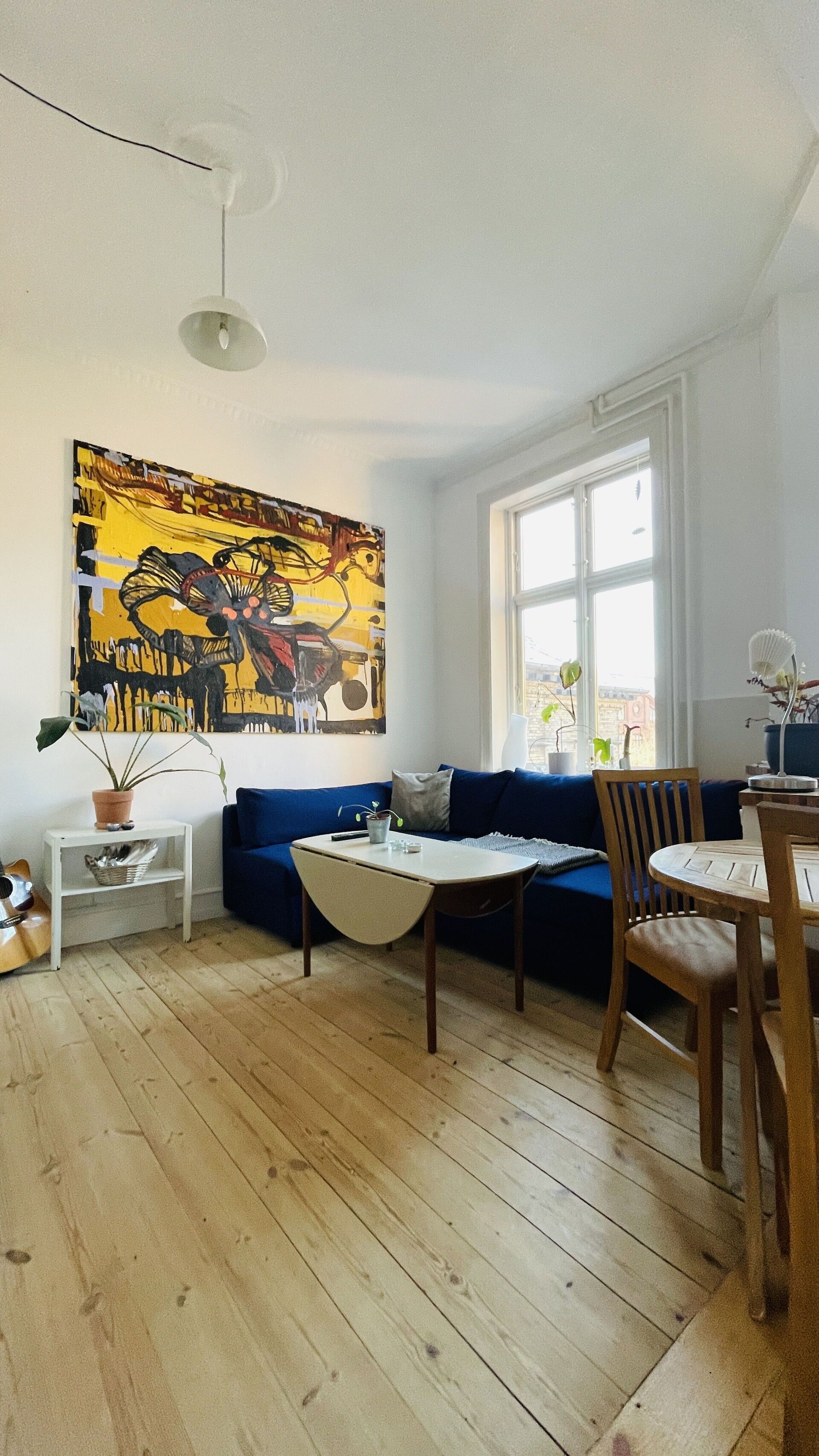 A modern living room with a blue sofa, wooden flooring, a white table, and a large abstract painting on the wall.