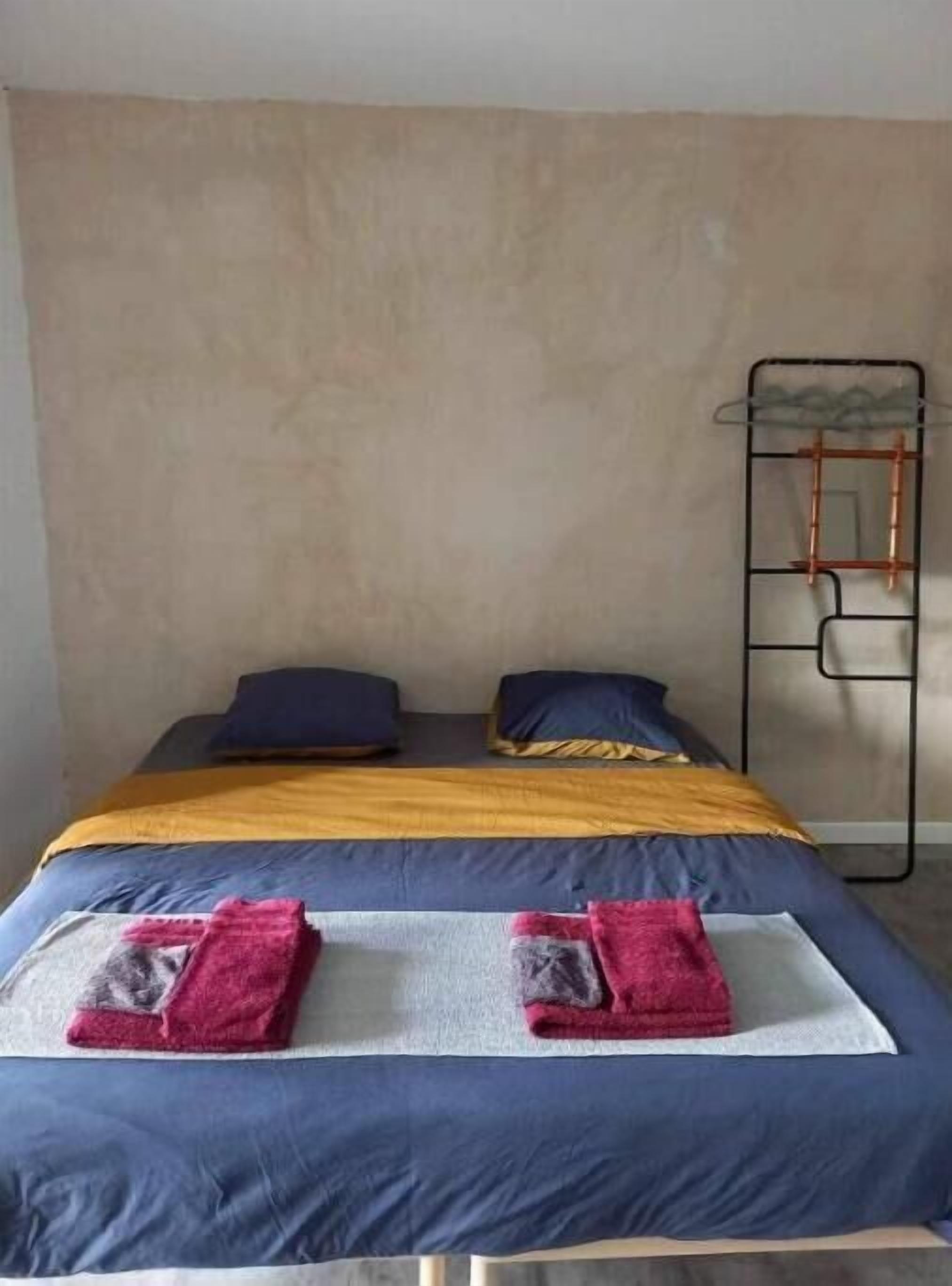 Un letto singolo con copriletto giallo e blu, due cuscini e un portascopevoli in metallo.