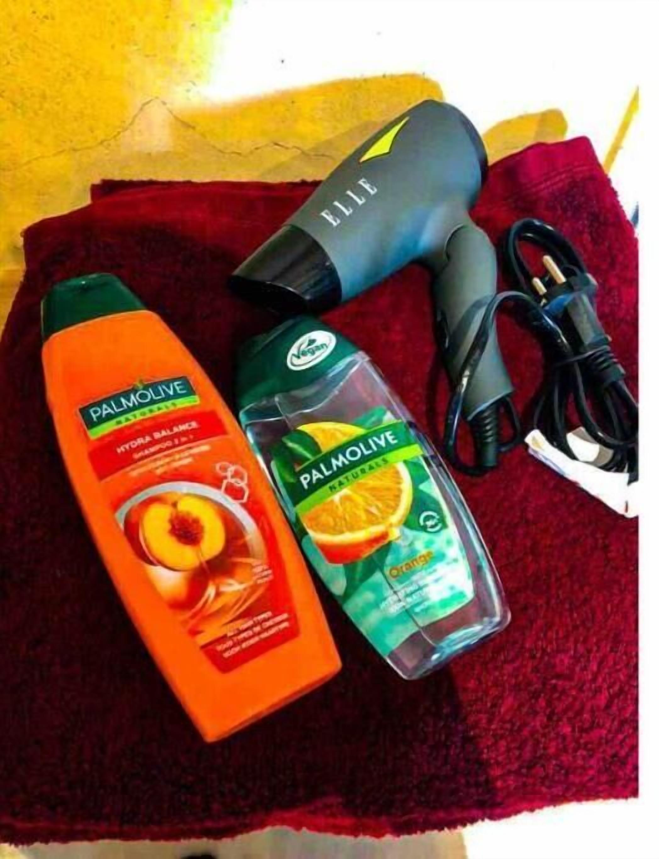 Ein rotes Handtuch, zwei Flaschen Palmolive Shampoo, ein Föhn und ein Stromkabel.