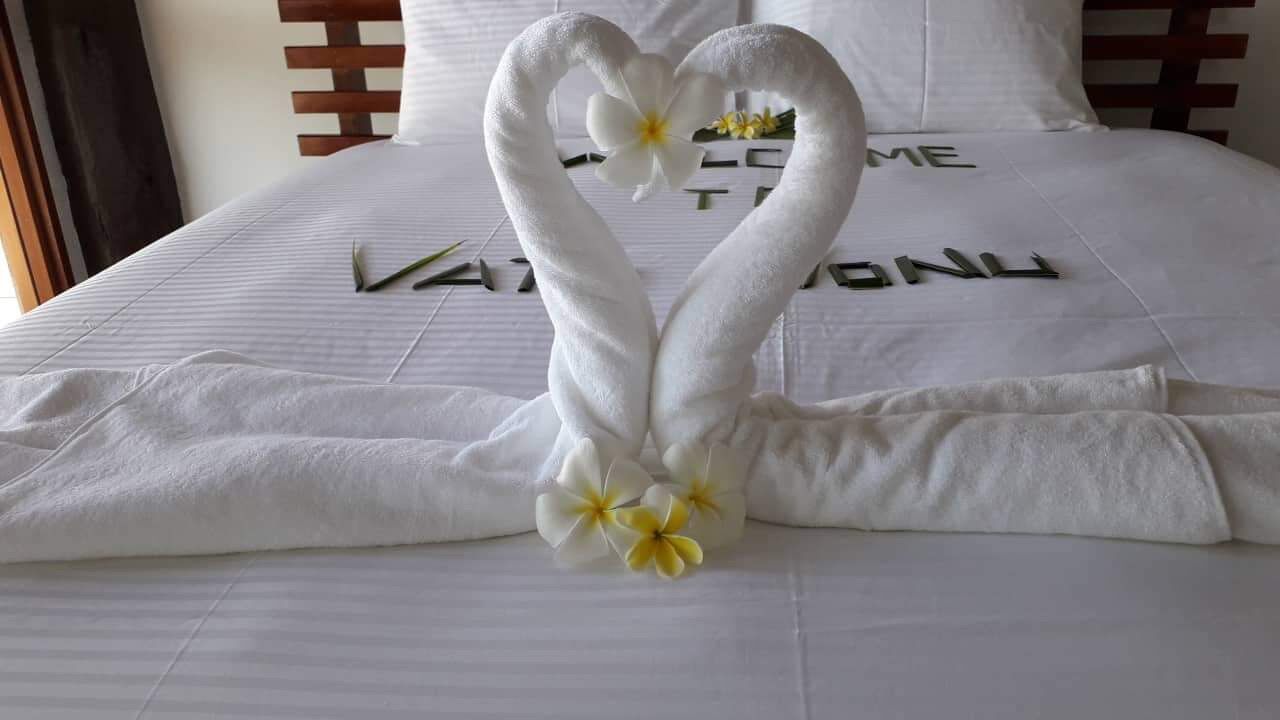 A bed with a heart-shaped towel arrangement and a welcome sign.