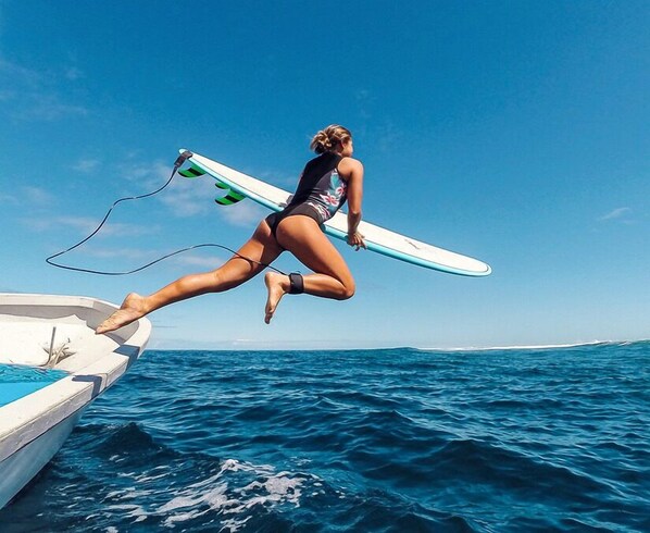 A person jumping off a boat into the ocean with a surfboard. - VatuVonu (Malolo Island)