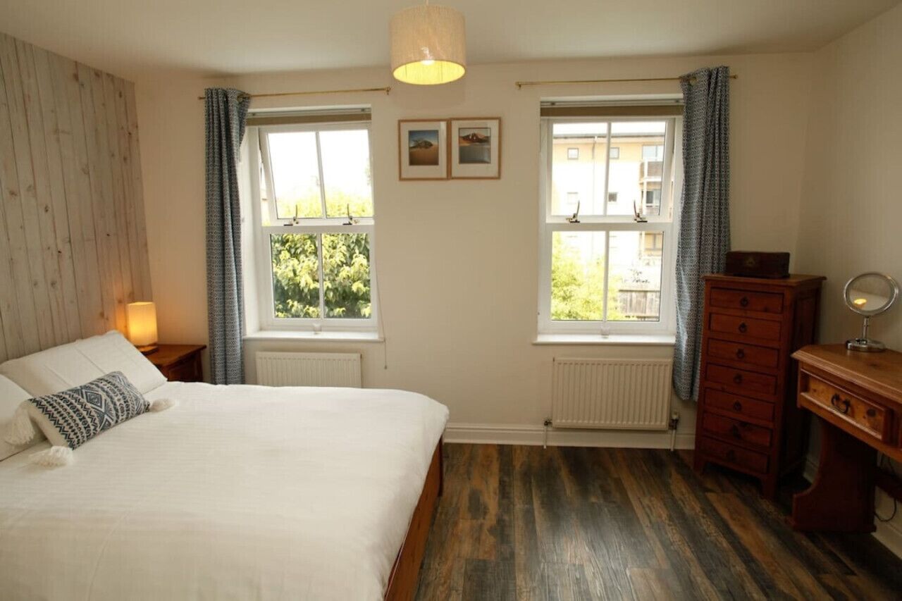 A bedroom with a bed, two windows, a dresser, and a lamp.
