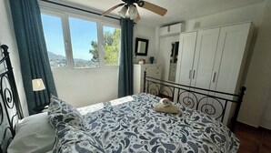 A bedroom with a bed, a ceiling fan, a dresser, and a window with curtains. - La Jacaranda Apartment, Sea Views, Games Room and Private Pool (Mijas)