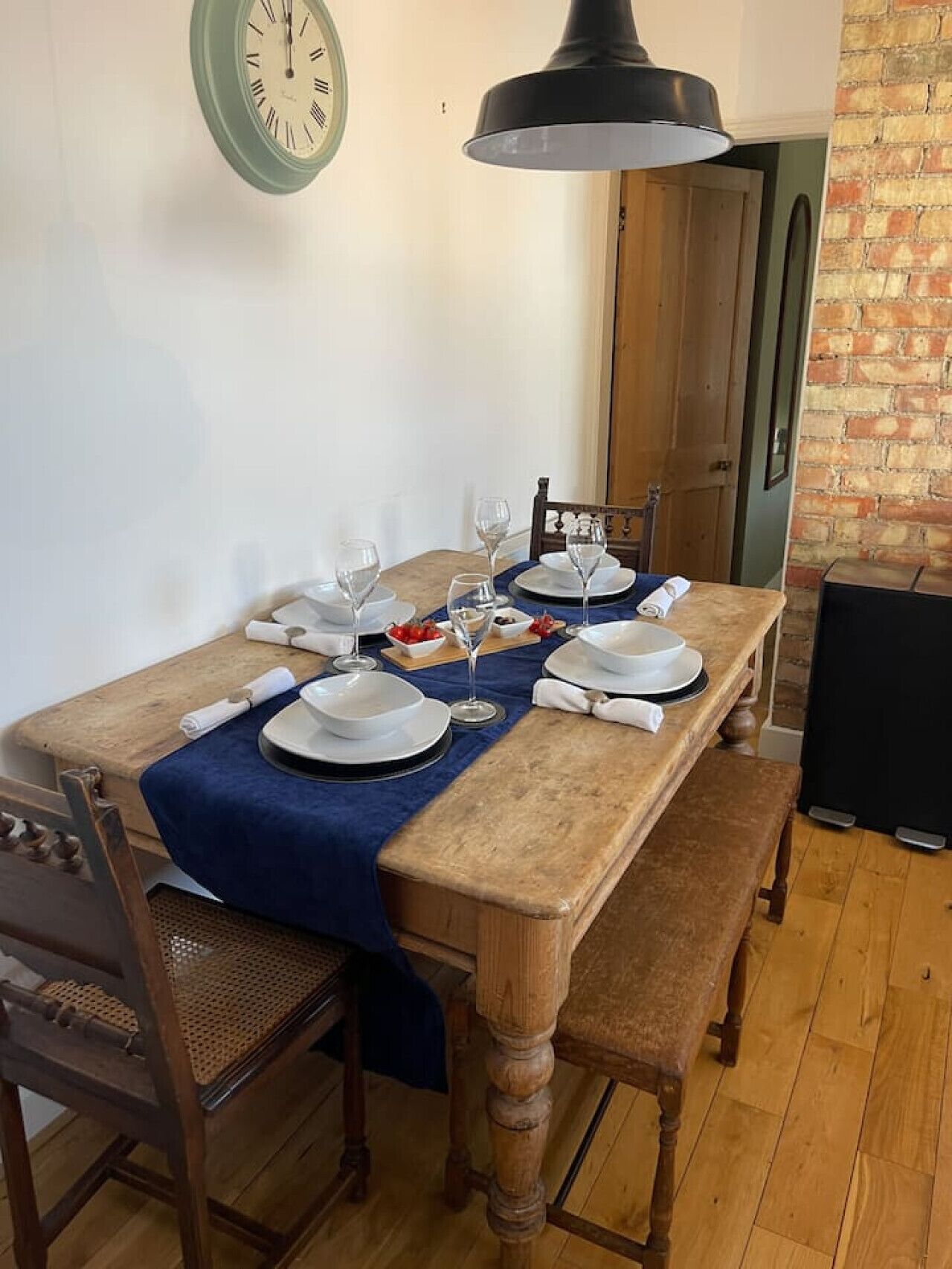 A dining table set with plates, glasses, and cutlery, a bench, and a clock on the wall.