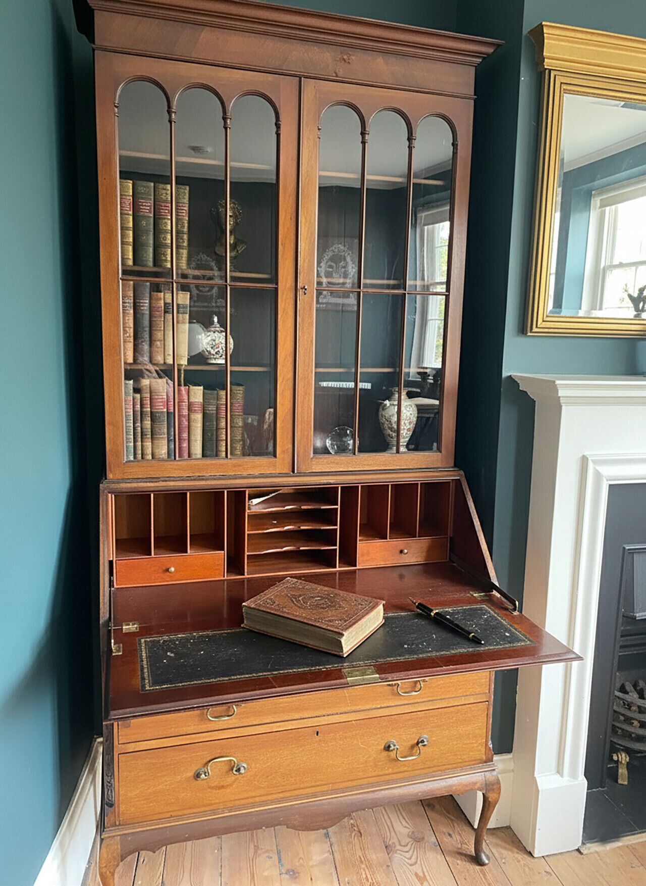 A wooden bookcase with multiple shelves and drawers, a mirror, and a fireplace in the background.