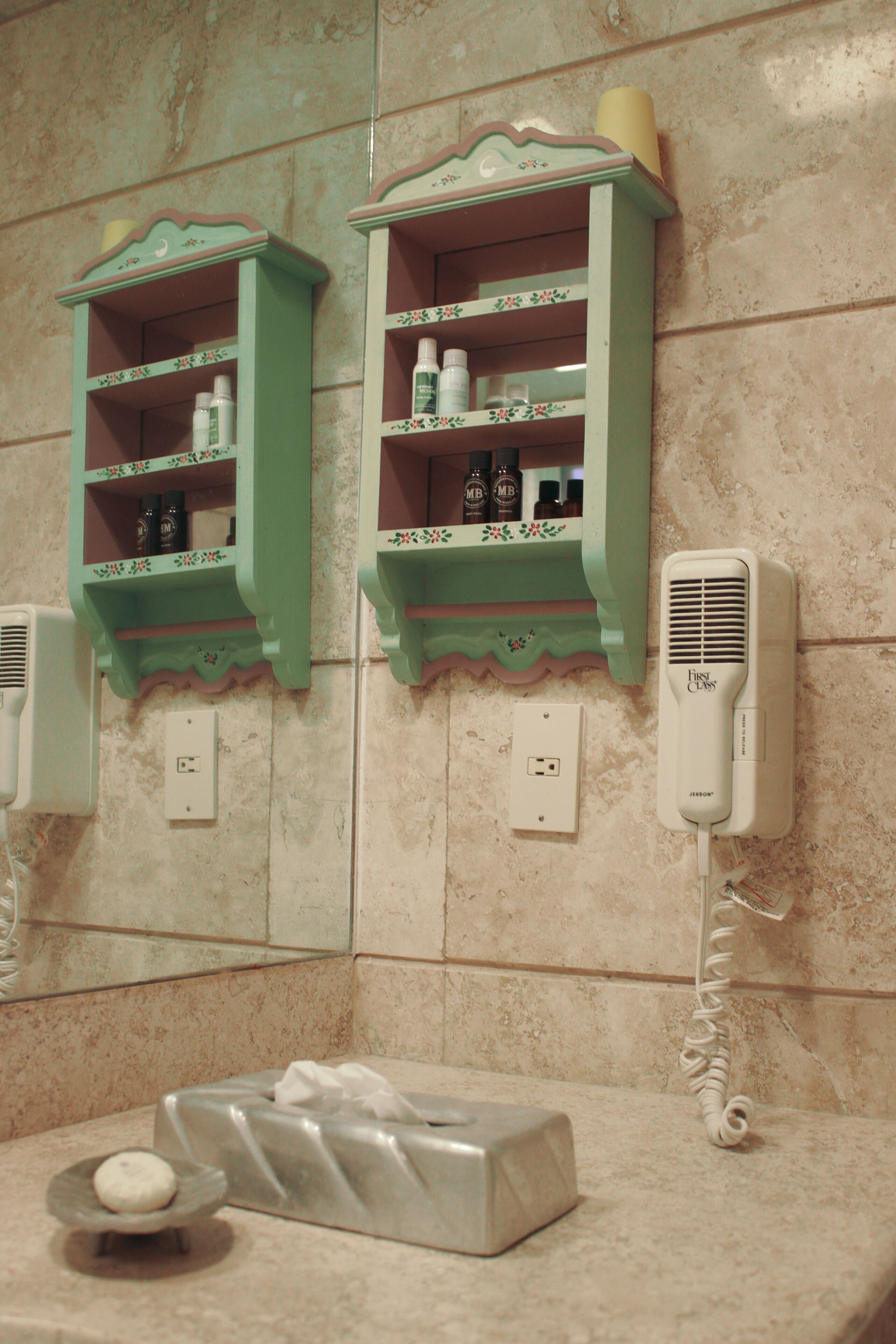 Un baño con dos repisas verdes que contienen artículos de tocador, un secador de pelo y una caja de pañuelos sobre el mostrador.