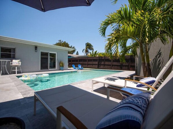 A backyard with a swimming pool, lounge chairs, and a palm tree. - Steps to Beach Heated Pool (Indian Rocks Beach)