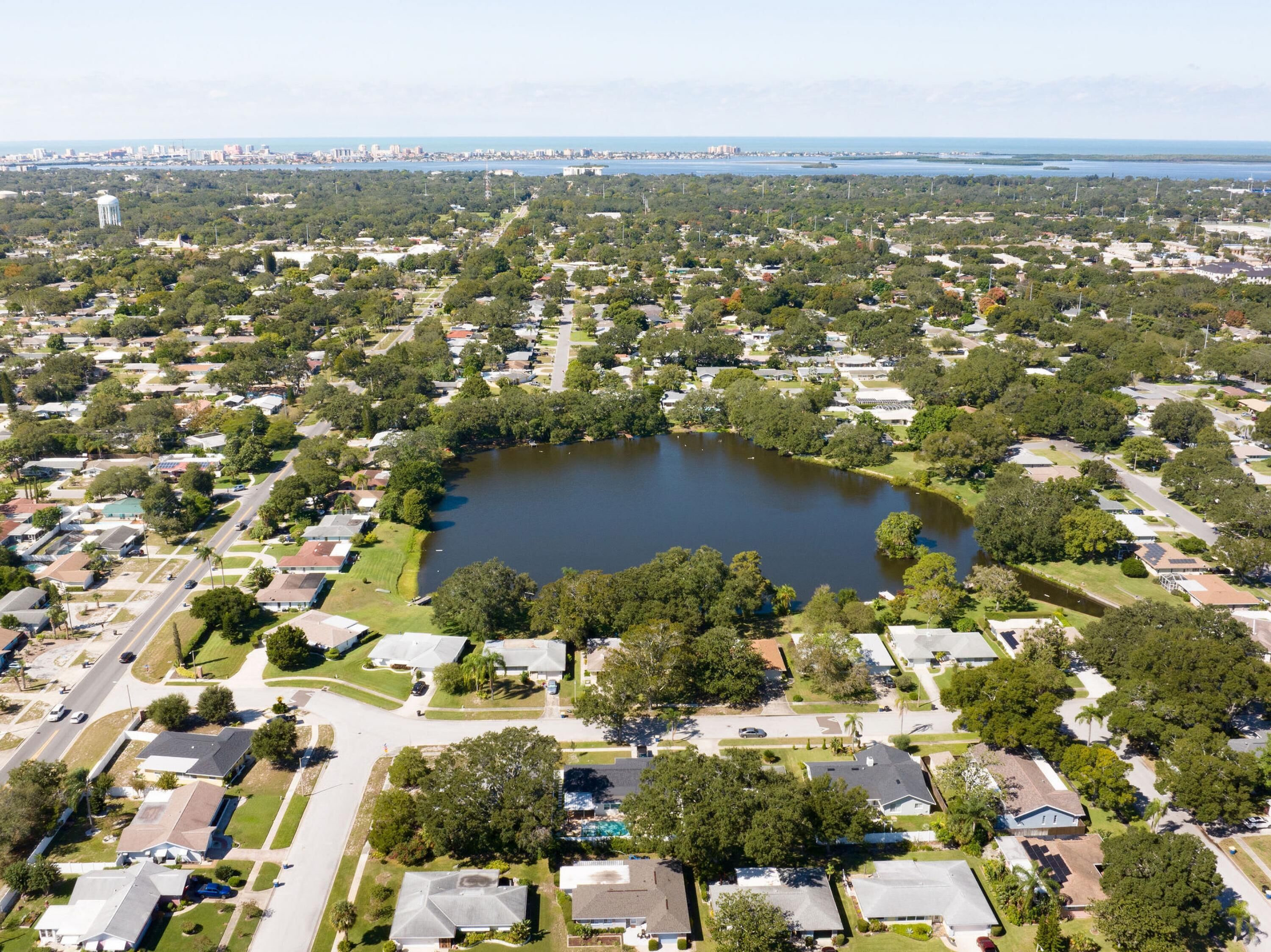 Une vue aérienne d’un quartier résidentiel avec un lac central, entouré de maisons, de routes et de verdure.