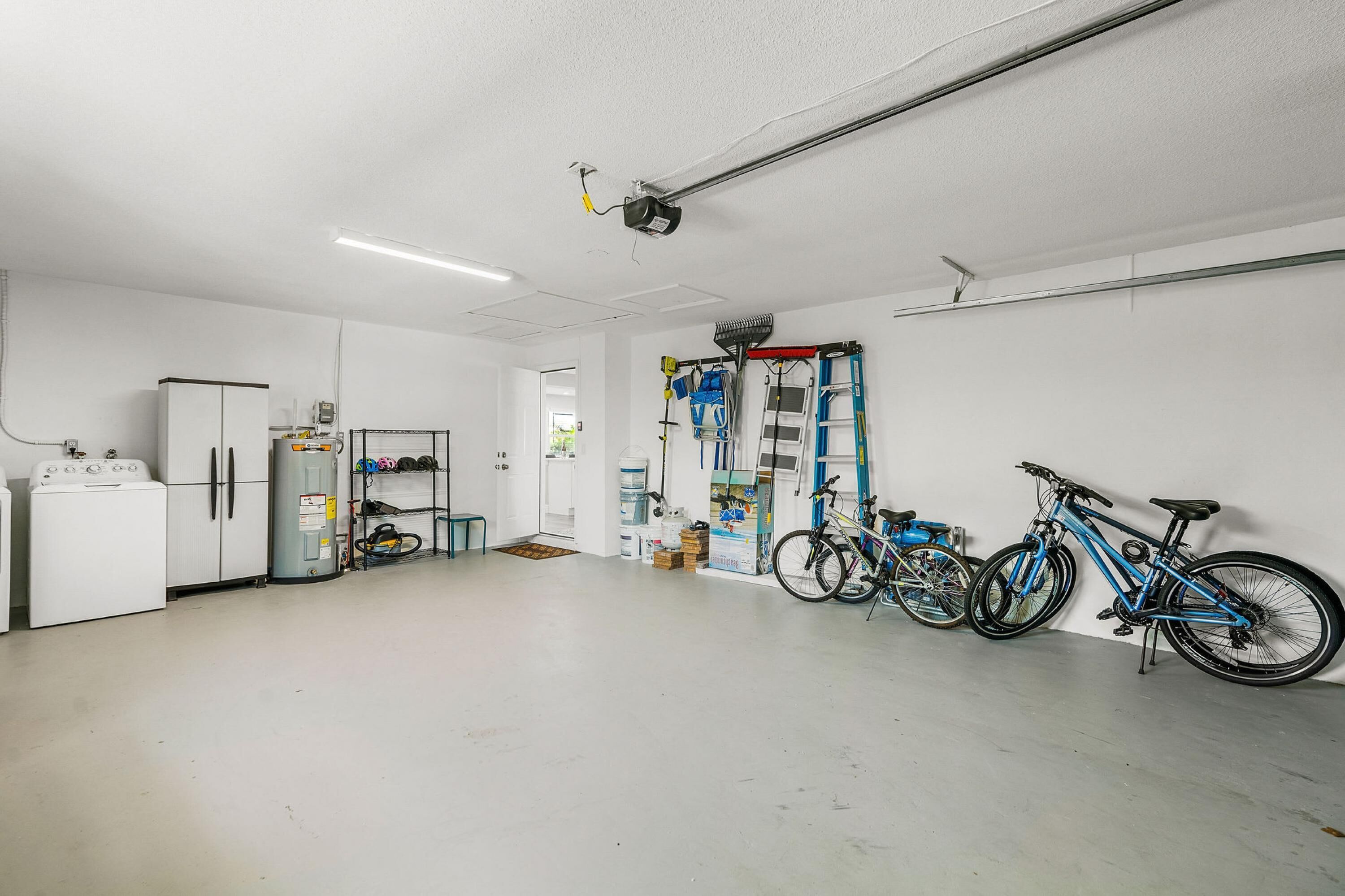 A clean, well-lit room with a washing machine, a refrigerator, and a bicycle rack with two bicycles.