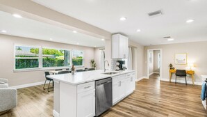 A modern kitchen with white cabinetry, a central island, and a dining area with a table and chairs. - Heated Pool Hot tub Clearwater Dunedin Pet Friendly (Clearwater)