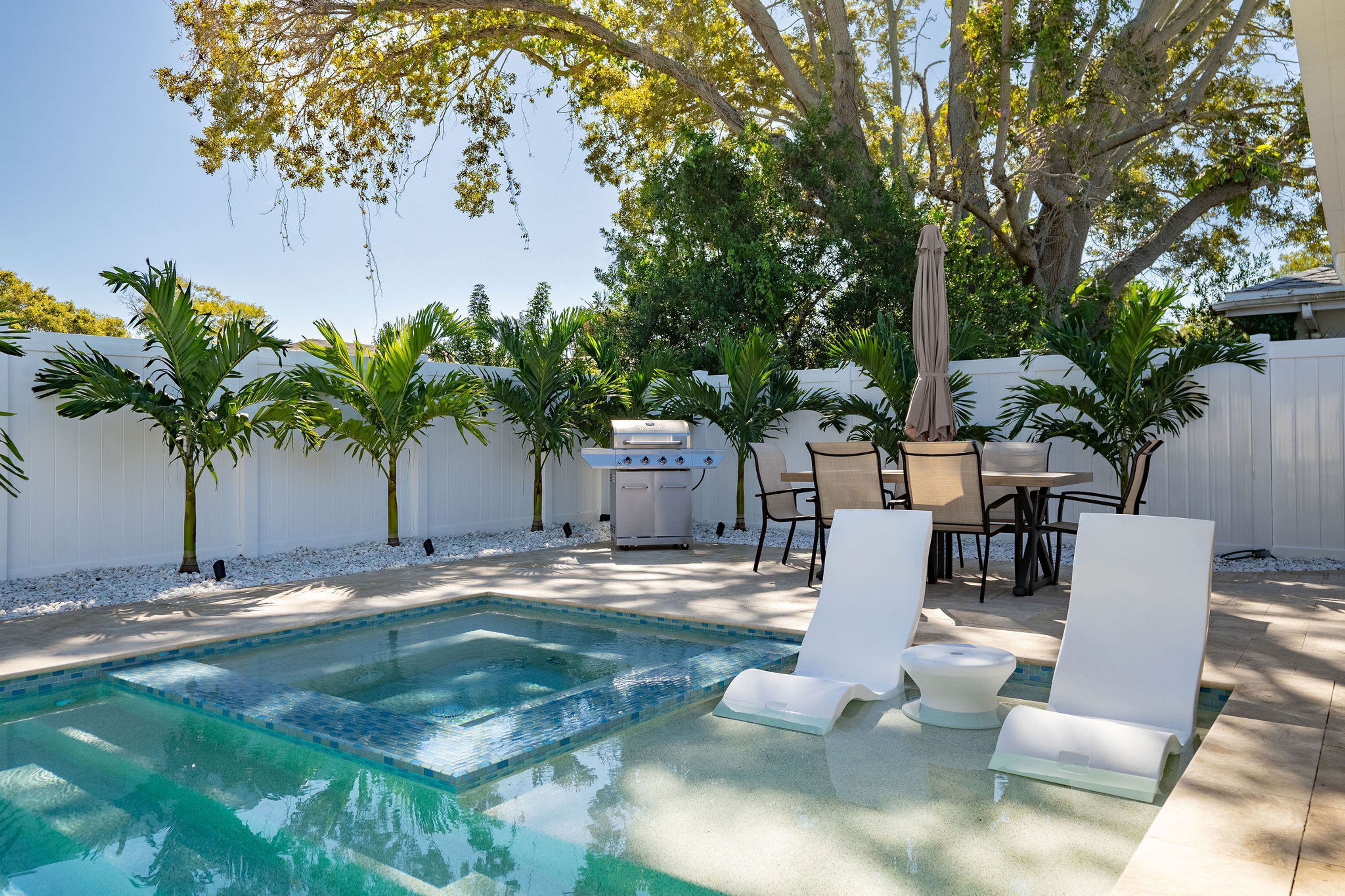 Une piscine avec des chaises longues, un barbecue et des palmiers.