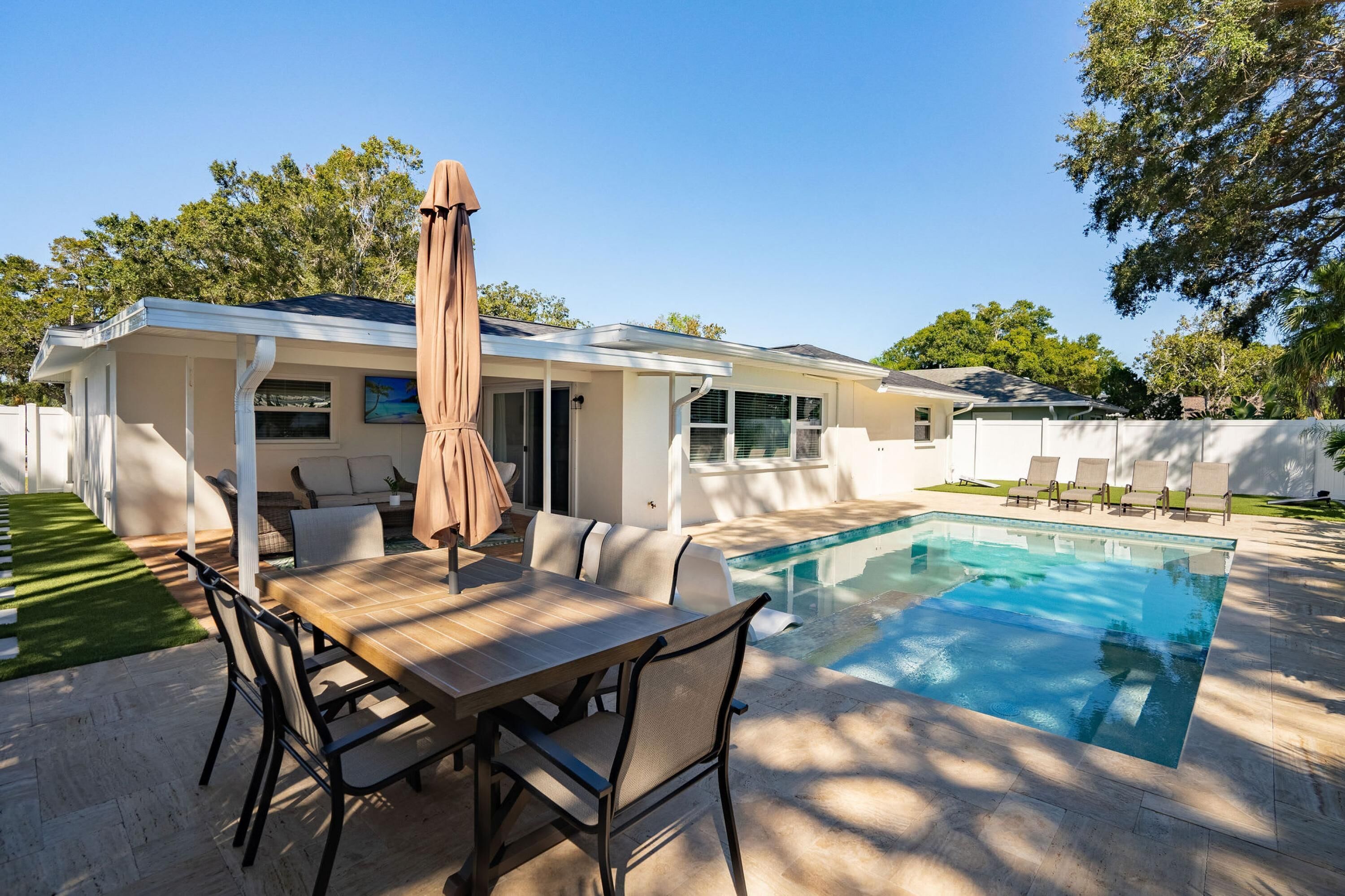 A poolside area with a dining table, chairs, and a covered umbrella.